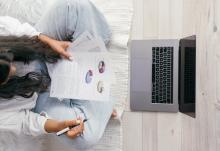 woman looking at research article seated on the floor with laptop